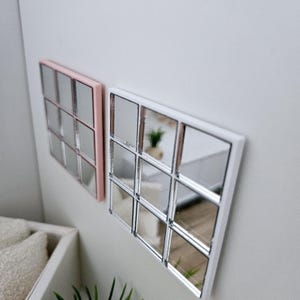 May include: Two square mirrors with a grid pattern. The mirror on the left has a pink frame and the mirror on the right has a white frame.