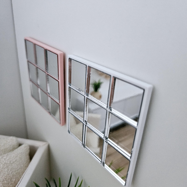 May include: Two square mirrors with a grid pattern. The mirror on the left has a pink frame and the mirror on the right has a white frame.