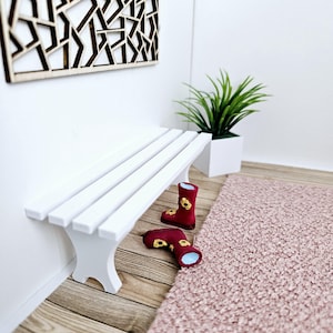 Può includere: Una panca di legno bianca con un tappeto rosa e stivali da pioggia rossi con dettagli di fiori gialli.