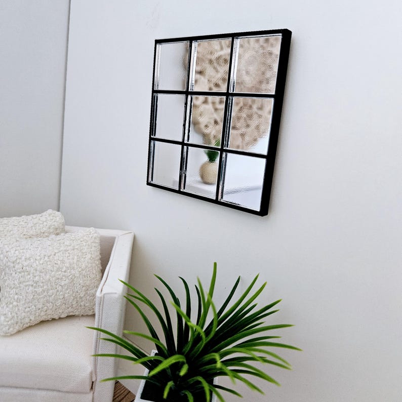 May include: A black framed square mirror with nine individual mirrored squares. The mirror is hanging on a white wall.