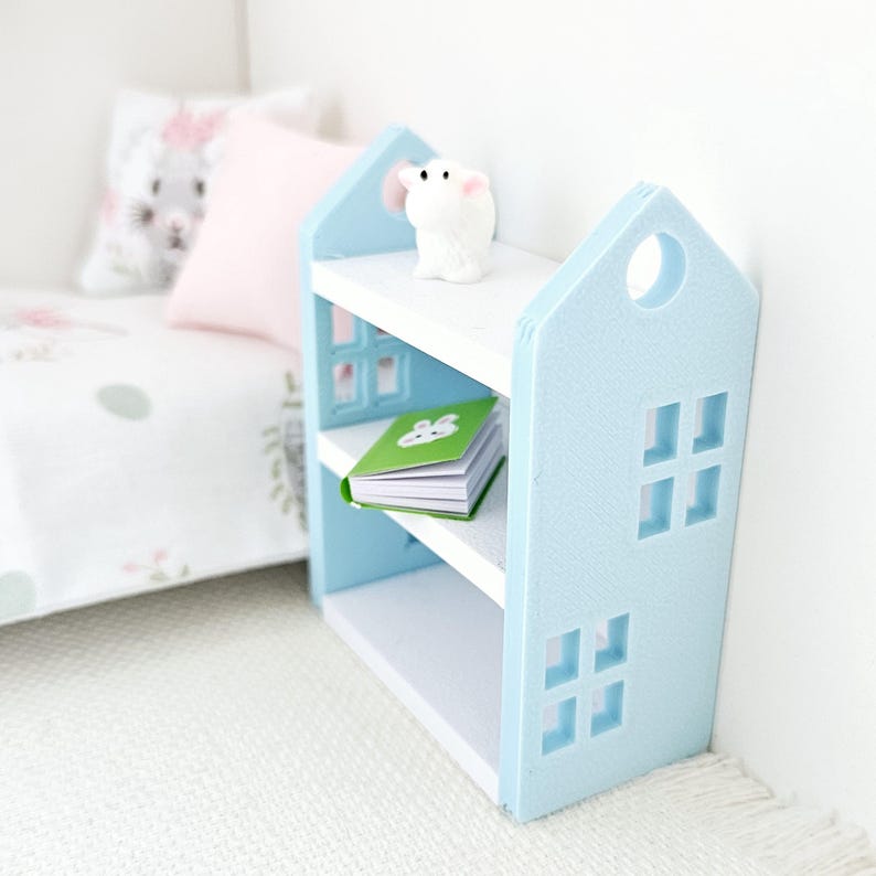 May include: A light blue bookshelf with three shelves, a white top, and a white rabbit figurine on the top shelf. A book with a green cover is on the middle shelf.