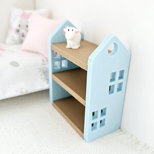 May include: A light blue bookshelf shaped like a house with two shelves and brown shelves. A small white figurine is on the top shelf.