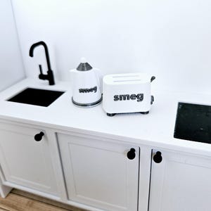 May include: White kitchen countertop with a black faucet, a white kettle with the word "Smeg" on it, and a white toaster with the word "Smeg" on it.