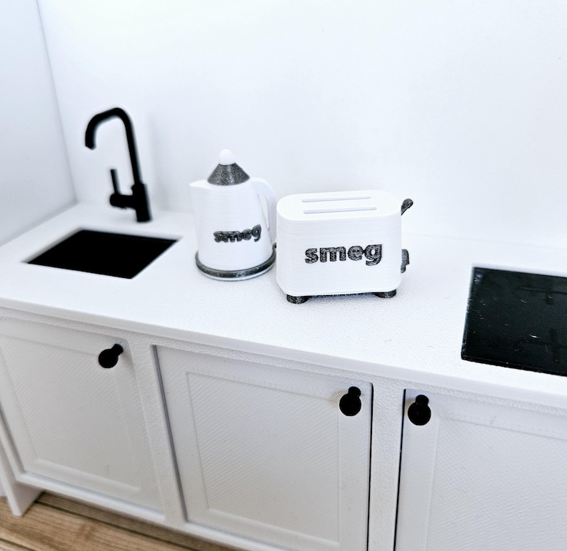 May include: White kitchen countertop with a black faucet, a white kettle with the word "Smeg" on it, and a white toaster with the word "Smeg" on it.