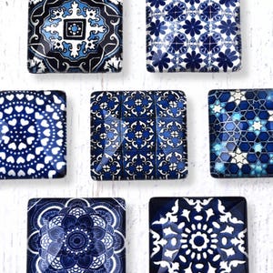 May include: Seven square magnets with intricate blue and white patterns. Designs include floral, geometric, and mandala-style motifs. The magnets are arranged on a white, textured surface, showcasing a variety of decorative styles.