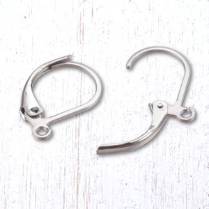 May include: Two silver-colored leverback earring findings. One is closed, showing the loop and lever mechanism. The other is open, displaying the hook and the hinge. The findings are on a white, textured surface.