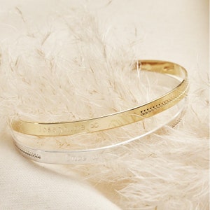 May include: Two thin gold and silver bangle bracelets with engraved text. The gold bracelet has the text "Josephine ∞" and the silver bracelet has the text "Once Upon A".