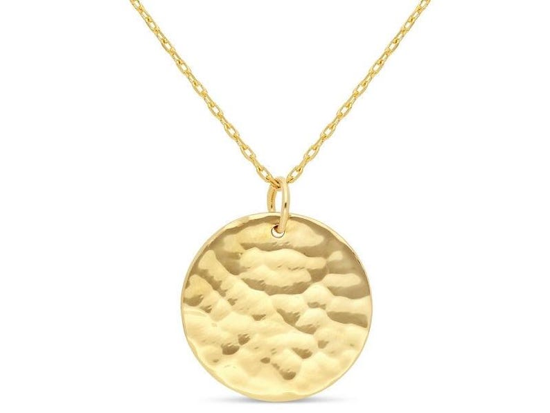 Puede incluir: Un collar de oro con un colgante redondo martillado. El colgante es un c&iacute;rculo simple con una superficie texturizada.
