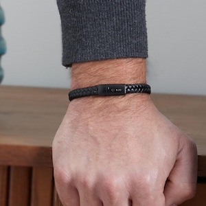 Puede incluir: Un brazalete de cuero negro con una placa de metal negro grabada con la palabra "Love".