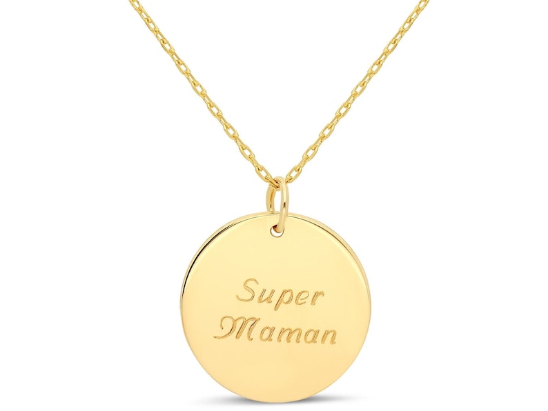 Puede incluir: Un collar de oro con un colgante redondo que dice "Super Maman" en cursiva.