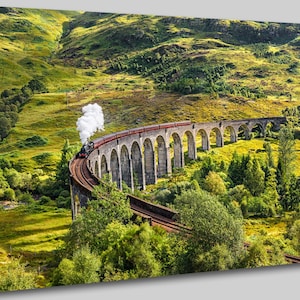 May include: A red and black steam train travels across a stone viaduct in a lush green valley. The train is emitting smoke and is surrounded by trees and hills.