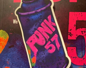 Pode incluir: Uma lata de tinta spray azul e roxa com contorno branco. A lata tem um rótulo rosa com a palavra "PUNK" e o número "57" nela.