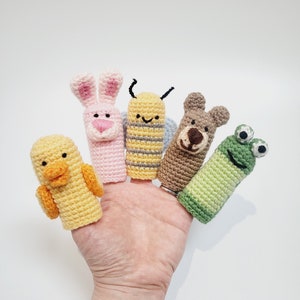 Può includere: Un gruppo di cinque marionette a dito fatte a mano all'uncinetto. Le marionette includono un'anatra gialla, un coniglietto rosa, un'ape gialla, un orso marrone e una rana verde. Ogni marionetta è progettata per essere indossata su un dito.