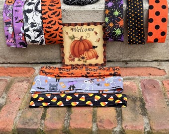 May include: A collection of ten fabric headbands featuring various Halloween patterns including bats, spiders, skeletons, candy corn, and polka dots, arranged around a square sign with a pumpkin illustration and the text Welcome.