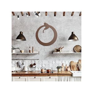 May include: A brown metal wall art piece depicting a snake eating its tail, forming a circle. The artwork is mounted on a textured gray wall in a kitchen setting, with shelves, pendant lights, and kitchenware visible.