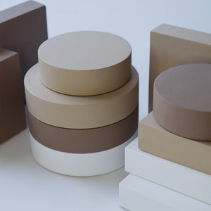 May include: A set of three stacked round platforms in beige, brown, and white, with a smaller beige platform on top. The platforms are arranged on a white surface, along with two rectangular beige platforms.