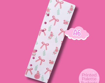 May include: A white A6 planner insert with a repeating pattern of pink bows, roses, and green leaves. The insert has three holes for binding. A pink cloud-shaped graphic with the text "A6" is on the right. The text "Printed Palette Budgets" is in a pink circle.