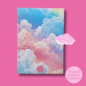 May include: A5-sized notebook cover featuring a dreamy cloudscape in shades of blue, pink, and white. The cover has a printed design of fluffy clouds and a rainbow. The text "Printed Palette Budgets" and "A5" are also visible.