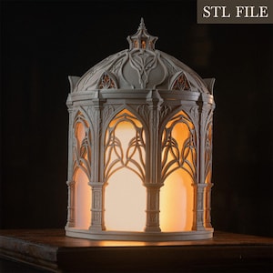 Puede incluir: Una linterna de color gris claro impresa en 3D con un intrincado dise&ntilde;o arquitect&oacute;nico g&oacute;tico, ventanas arqueadas y un techo abovedado. La estructura est&aacute; iluminada desde el interior, emitiendo un c&aacute;lido resplandor naranja. El texto dice STL FILE.