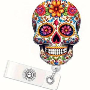 May include: A colorful, Day of the Dead-themed badge reel featuring a detailed sugar skull design. The skull is adorned with vibrant floral patterns in red, orange, yellow, blue, and pink. A white plastic reel with a metal clip is attached.