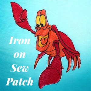May include: Embroidered iron-on or sew-on patch featuring a cartoon crab in shades of red, orange, and yellow. The crab is smiling with one claw raised. The words "Iron on Sew Patch" are printed in white.