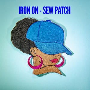 May include: Embroidered patch featuring a Black woman wearing a blue baseball cap and pink hoop earrings. The patch has black hair and red lips. The text "IRON ON - SEW PATCH" is displayed in blue at the top.