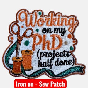 May include: Embroidered patch with the text "Working on my PhD (projects half done)". The patch features scissors, spools of thread, and a green ribbon. The text "Iron on - Sew Patch" is at the bottom.