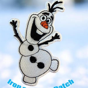 May include: Embroidered patch featuring Olaf from Frozen. The patch is white with black and orange accents, depicting Olaf with a smiling face and outstretched arms. The text "Iron on - Sew Patch" is printed in blue.