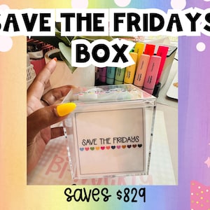 May include: A clear acrylic square box featuring a white label on the front with the text SAVE THE FRIDAYS in black lettering, underlined by a row of small colorful hearts. The box contains various items and is held against a desk background.