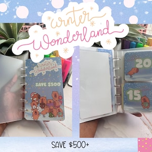 May include: A clear, open binder with a Winter Wonderland theme. The binder contains cards with illustrations of bears and the text "SAVE £500". Additional cards show numbers 15 and 20 with bear illustrations. The background is light blue with white polka dots.