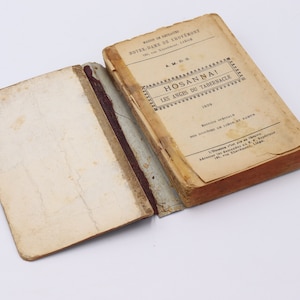 Puede incluir: Un libro antiguo titulado "HOSANNAI LES ANGES DU TABERNACLE" con el año 1926 impreso en la portada. El libro está encuadernado en cuero marrón y tiene un aspecto desgastado y envejecido.
