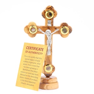May include: A small wooden cross crafted from olive wood from Bethlehem, featuring a silver Jesus figure and four small glass vials. The cross stands on a wooden base and includes a certificate of authenticity.