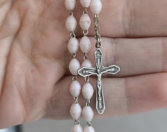 May include: A white rosary with a silver crucifix. The beads are oval shaped and the crucifix has a figure of Jesus on it.