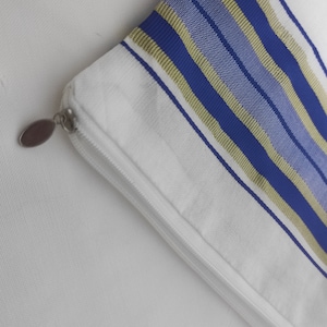 May include: A white zippered pouch with blue and gold stripes. The pouch is made of a soft fabric and has a zipper closure.