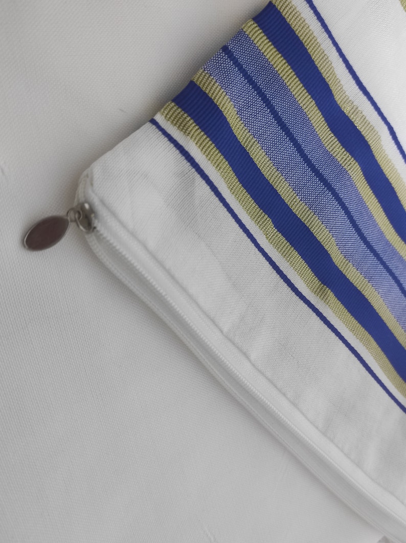 May include: A white zippered pouch with blue and gold stripes. The pouch is made of a soft fabric and has a zipper closure.
