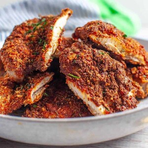 May include: Close-up of a plate of crispy, golden brown chicken tenders. The chicken is coated in a flavorful, spiced breading and is arranged in a pile on a white plate.