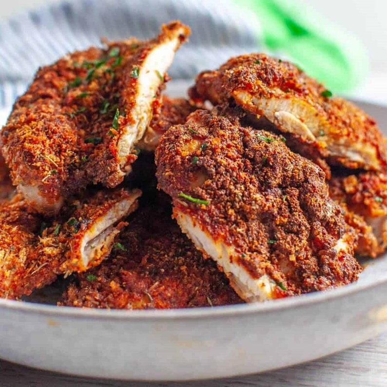 May include: Close-up of a plate of crispy, golden brown chicken tenders. The chicken is coated in a flavorful, spiced breading and is arranged in a pile on a white plate.