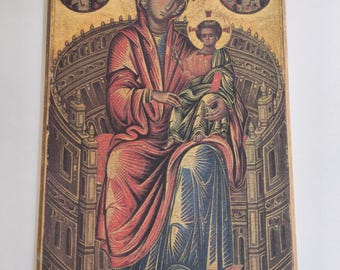 May include: A religious icon depicting a seated figure in red and blue robes holding a child. Two circular images of angels flank the central figures. The background is gold with architectural details.