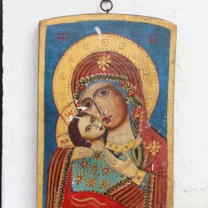 Peut inclure: Une icône en bois vintage représentant la Vierge Marie et l'enfant Jésus. L'icône est peinte dans des couleurs vives, notamment le rouge, le bleu, l'or et le blanc. La Vierge Marie porte une robe bleue et rouge, et l'enfant Jésus porte une robe blanche. L'icône est entourée d'un cadre doré.