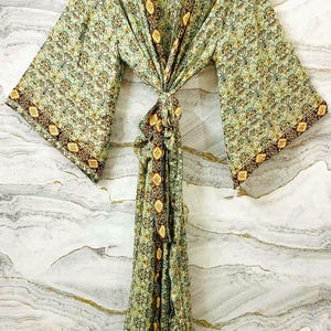 May include: A long-sleeved kimono robe featuring a light green base with an intricate repeating floral pattern in shades of teal and gold. The garment includes a dark brown border with a yellow diamond motif along the front opening and cuffs.