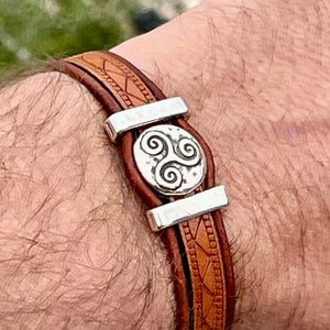 May include: A brown leather bracelet with a silver Celtic knot design. The bracelet has two silver clasps.