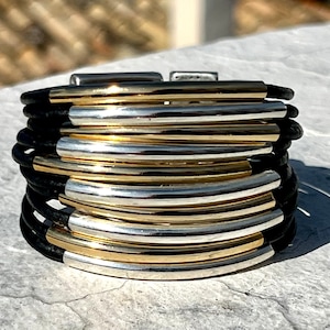 Peut inclure: Un bracelet en cuir noir avec plusieurs bandes dorées et argentées. Le bracelet est composé de plusieurs couches de cuir et de métal.