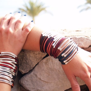 May include: A stack of leather bracelets with silver accents. The bracelets are in various shades of brown, red, and blue.