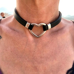 Puede incluir: Un collar de cuero negro con un colgante de corazón plateado.