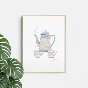 May include: A framed wall art print featuring a watercolor illustration of a blue and white teapot, a matching teacup, and a small creamer pitcher. The design includes delicate floral patterns and swirling steam lines on a white background.