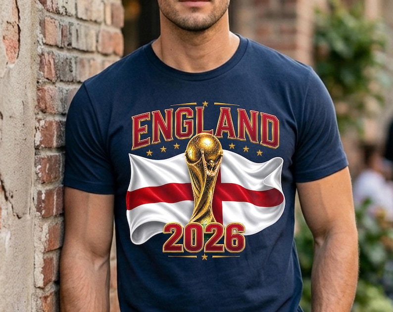 May include: Navy blue t-shirt featuring the word "ENGLAND" in red and gold lettering, with a gold trophy and the England flag. The number "2026" is displayed in red and gold below the flag.
