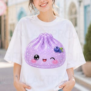 May include: A white short-sleeved t-shirt featuring a large, glittery purple dumpling graphic on the front. The dumpling has a cute, winking face with rosy cheeks and is decorated with a small cluster of blue blueberries and green leaves.