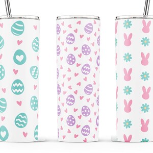May include: Three stainless steel tumblers with different Easter-themed designs. The first tumbler has a pattern of teal eggs and pink hearts. The second tumbler has a pattern of purple eggs and pink hearts. The third tumbler has a pattern of pink bunnies and teal flowers.