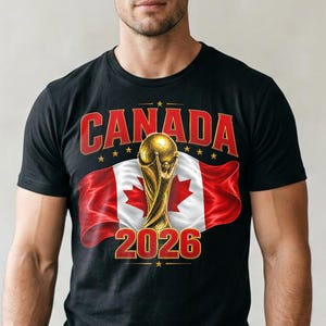 May include: Black t-shirt featuring the word "CANADA" in red, with a gold trophy and the number "2026" in gold. The Canadian flag is in the background. The shirt is a crew neck.