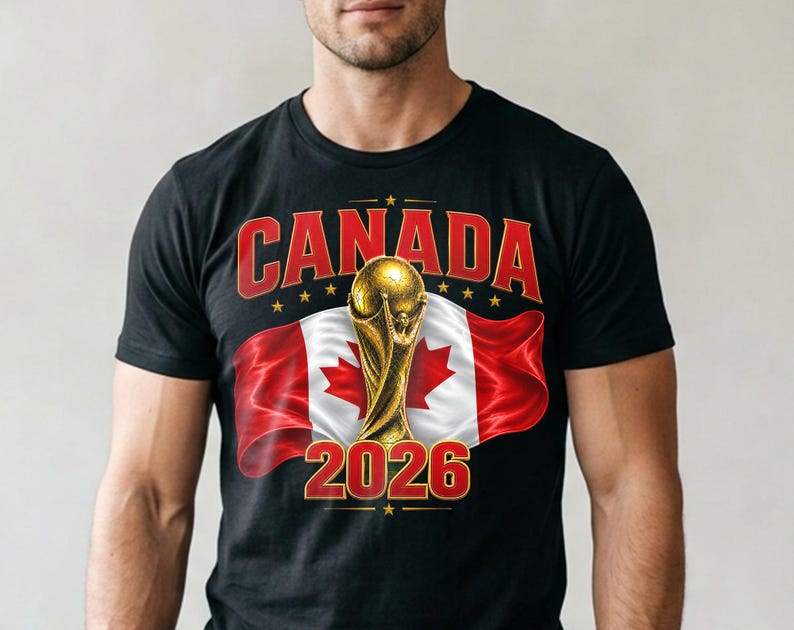 May include: Black t-shirt featuring the word "CANADA" in red, with a gold trophy and the number "2026" in gold. The Canadian flag is in the background. The shirt is a crew neck.